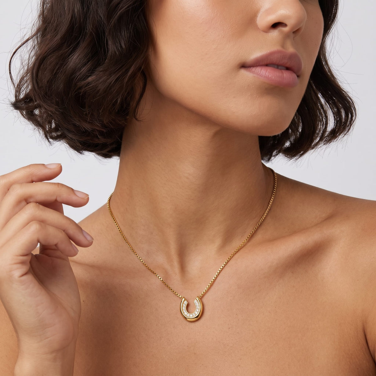 Woman wearing the Léonore horseshoe crystal gold necklace at the collarbone touching her short dark hair
