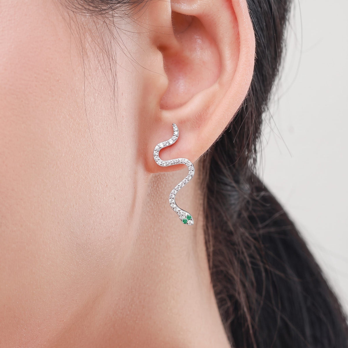 Woman wearing the Liana crystal snake earring winding down from her lobe, green stone at the head