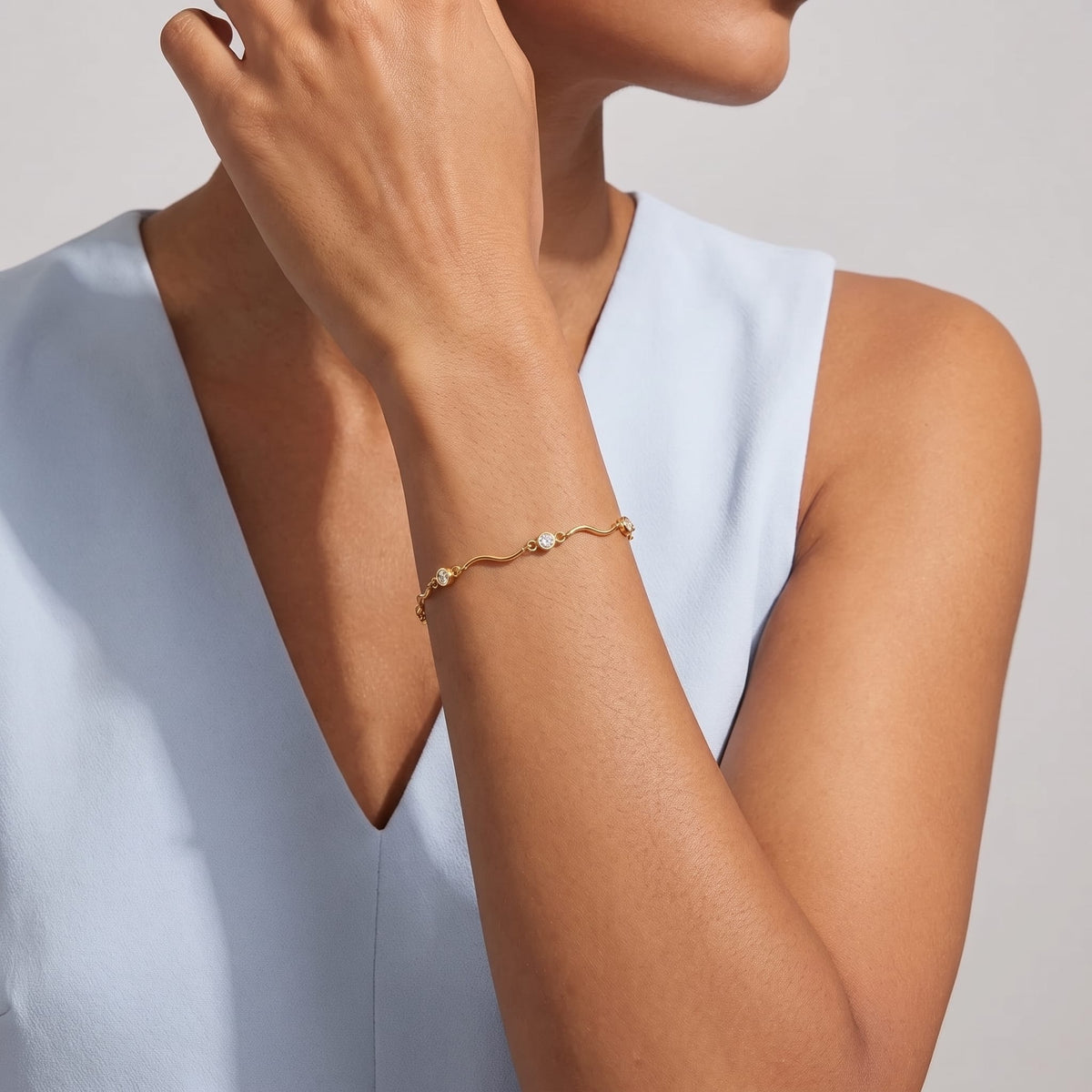 Woman wearing the Luna wave crystal gold bracelet on the wrist in a blue vest