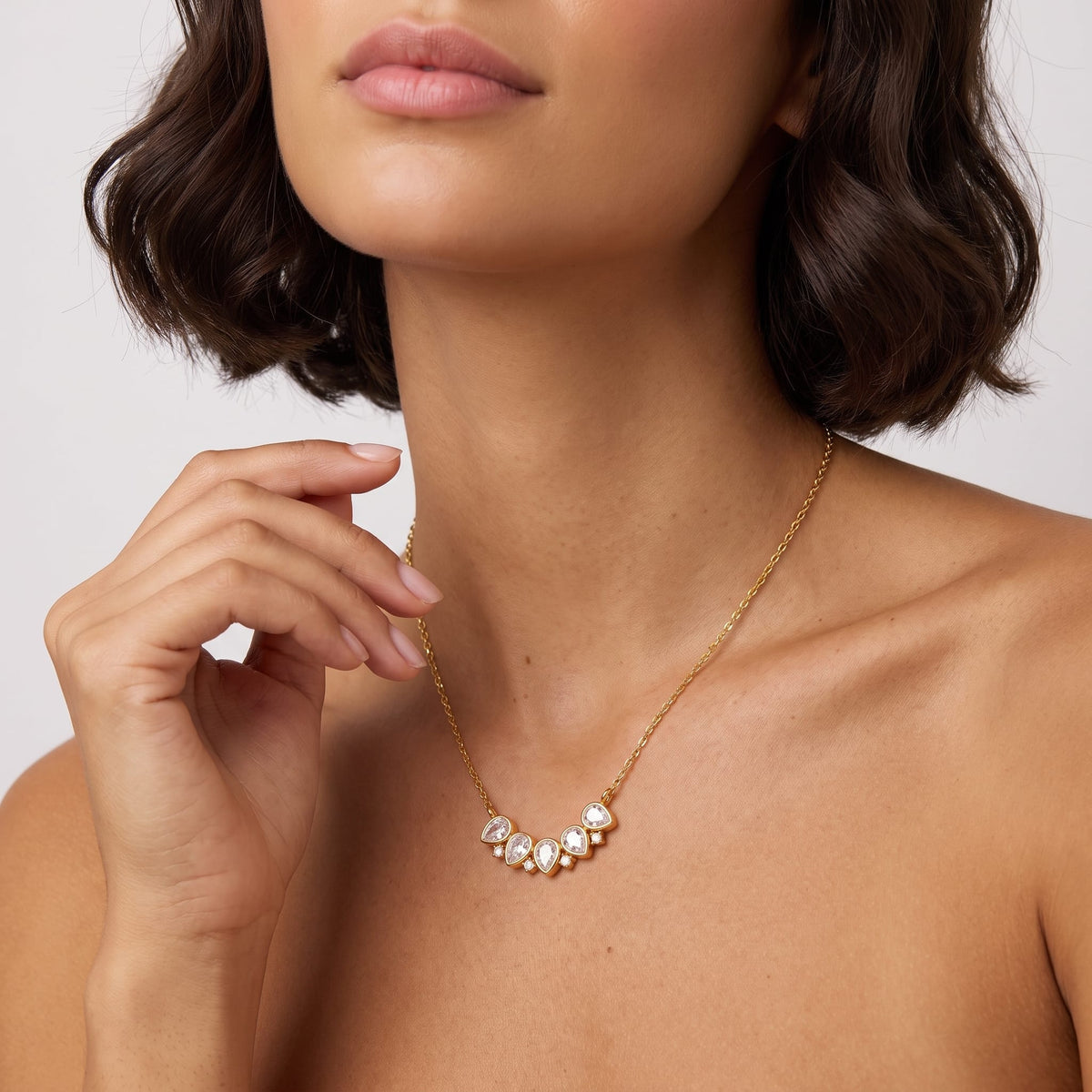Woman wearing the Mélisande crystal crescent gold necklace at her collarbone posing against light backdrop