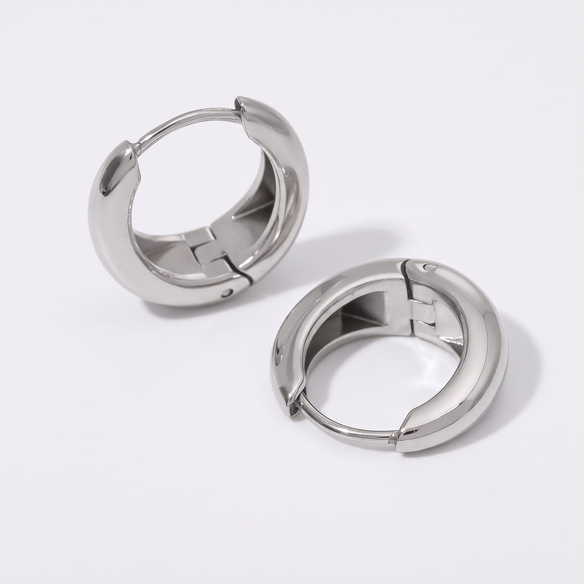 Nina dome huggie silver earrings on a plain white surface