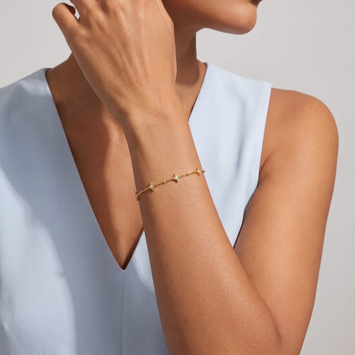 Woman wearing the Océane star station gold bracelet on the wrist in a light blue top
