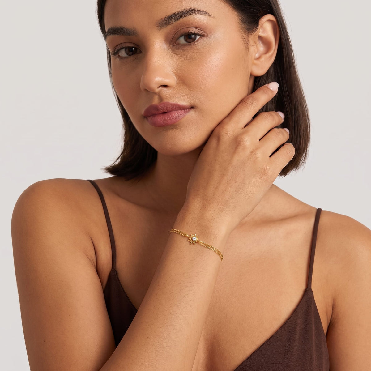 Woman wearing the Olivia crystal sun gold bracelet on the wrist wearing a brown camisole top