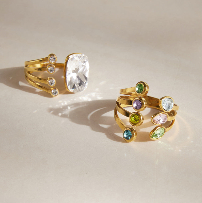 Olivia cushion crystal gold ring beside the Giulia pastel crystal ring on a cream surface