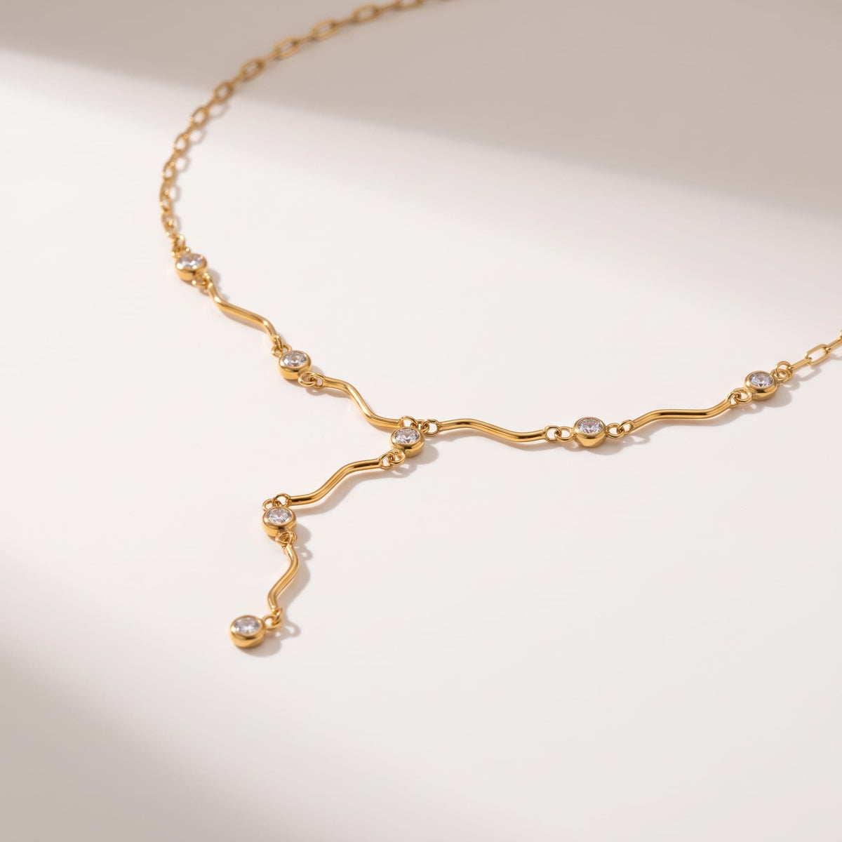 Ondine wave crystal gold necklace on a smooth cream surface with soft shadows