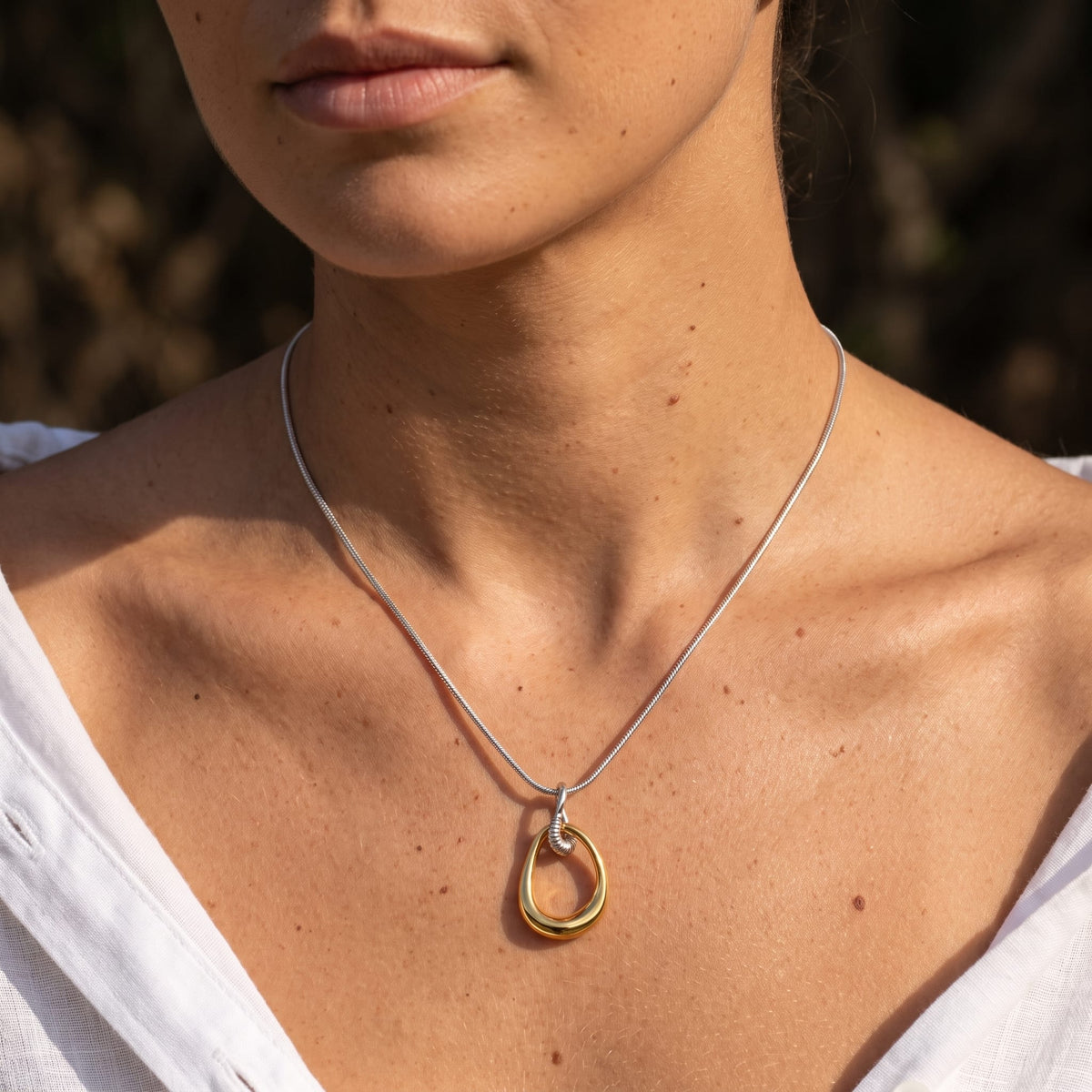 Woman wearing the Oriane open teardrop two-tone necklace at the collarbone with a white linen shirt