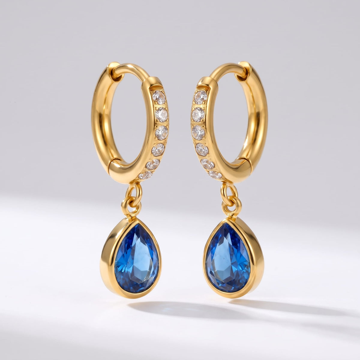 Paola blue teardrop gold earrings on a plain white background