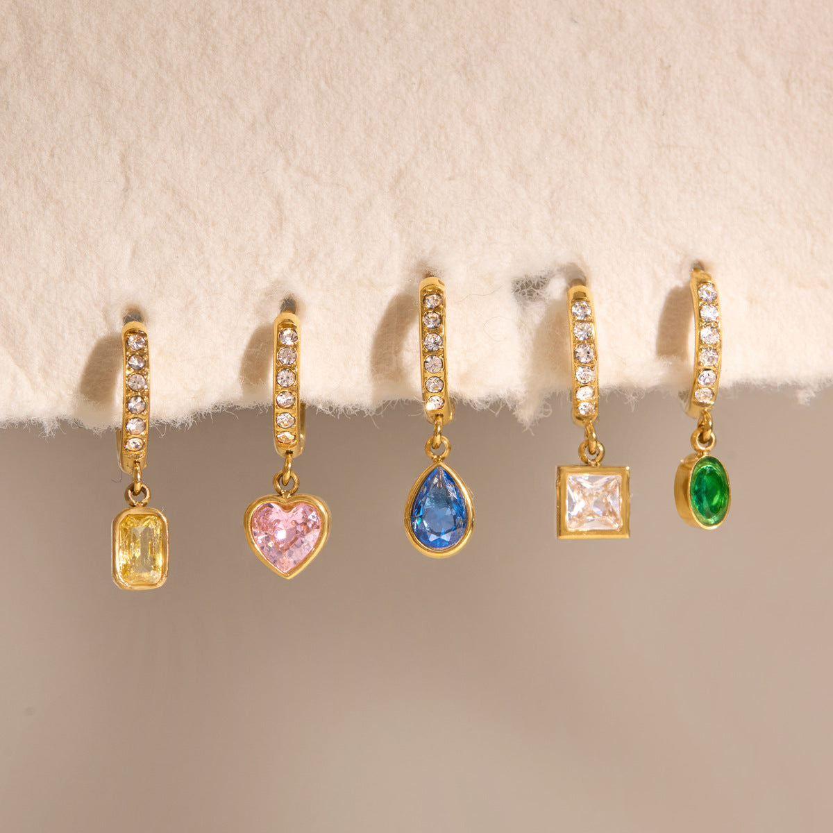 Paola green oval huggie at the end of a row of five colored crystal earrings