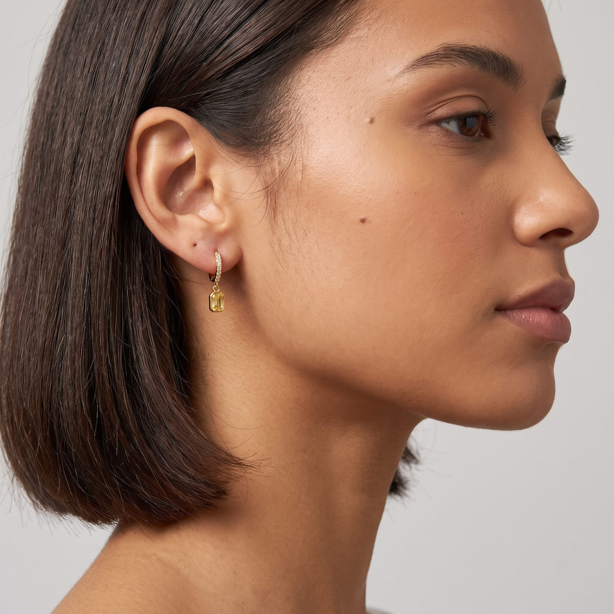 Woman wearing the Paola yellow octagon gold earrings on the ear facing right