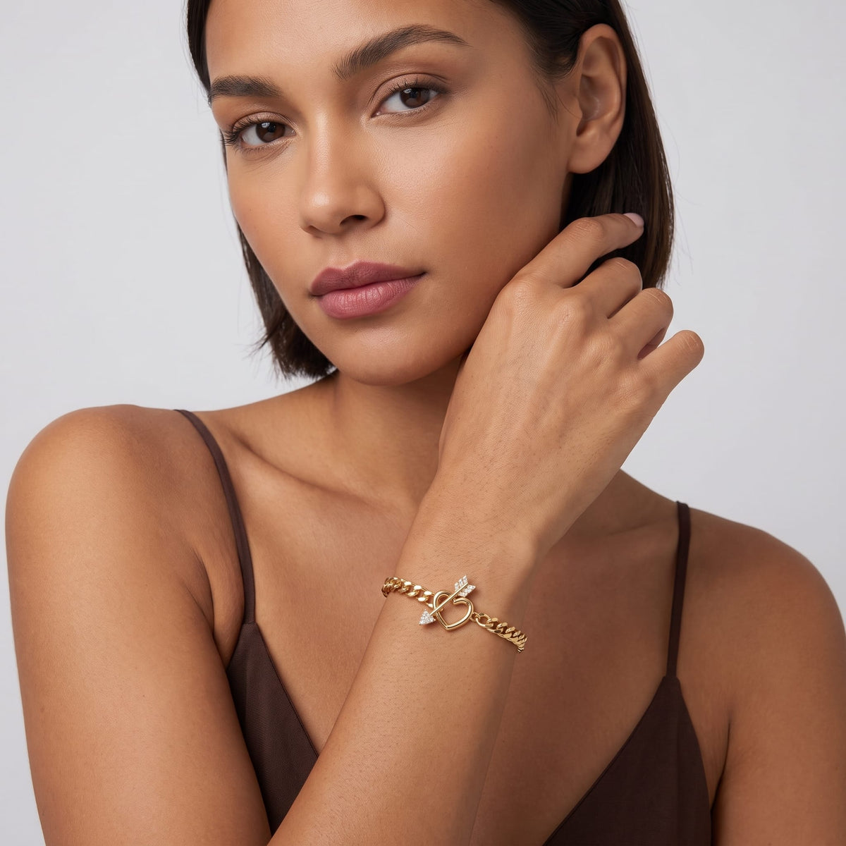 Woman wearing the Rafaella heart arrow gold bracelet on the wrist wearing a dark brown top