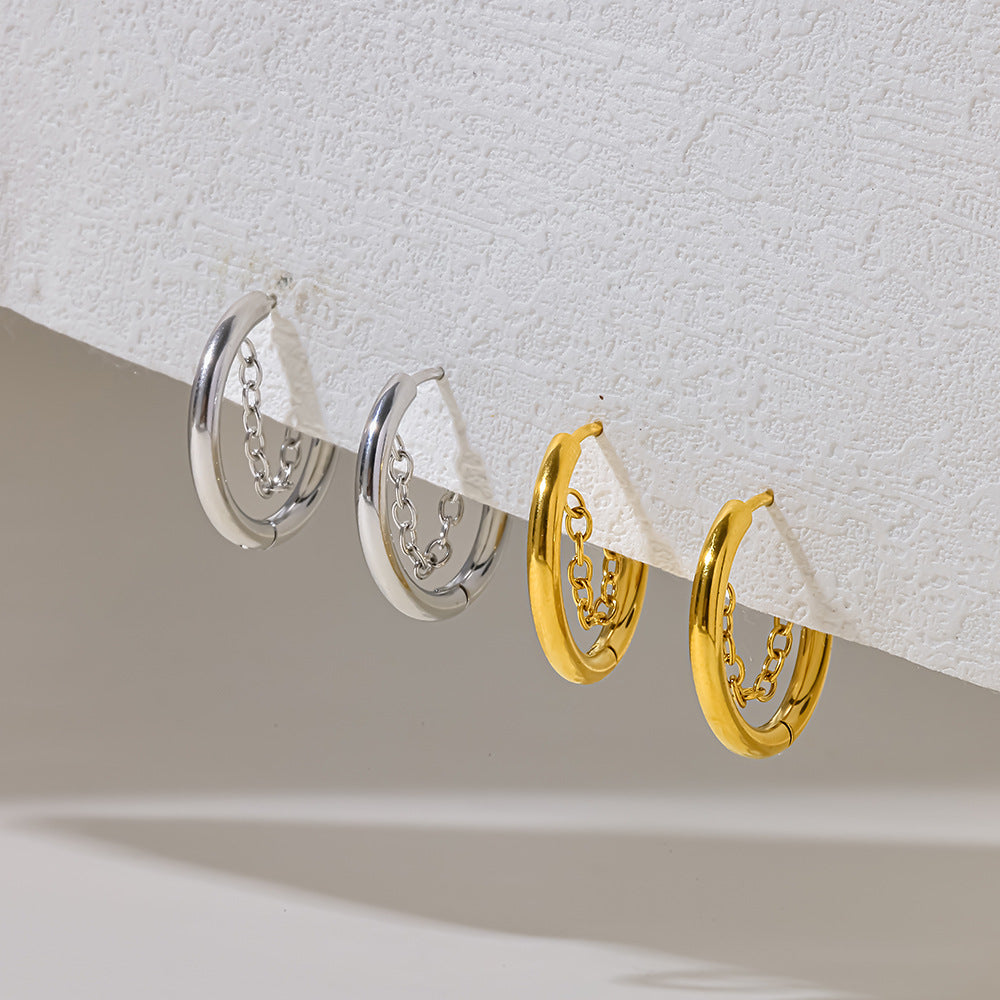 Gold Romy chain hoops hanging from a textured white ledge to the right of the silver pair