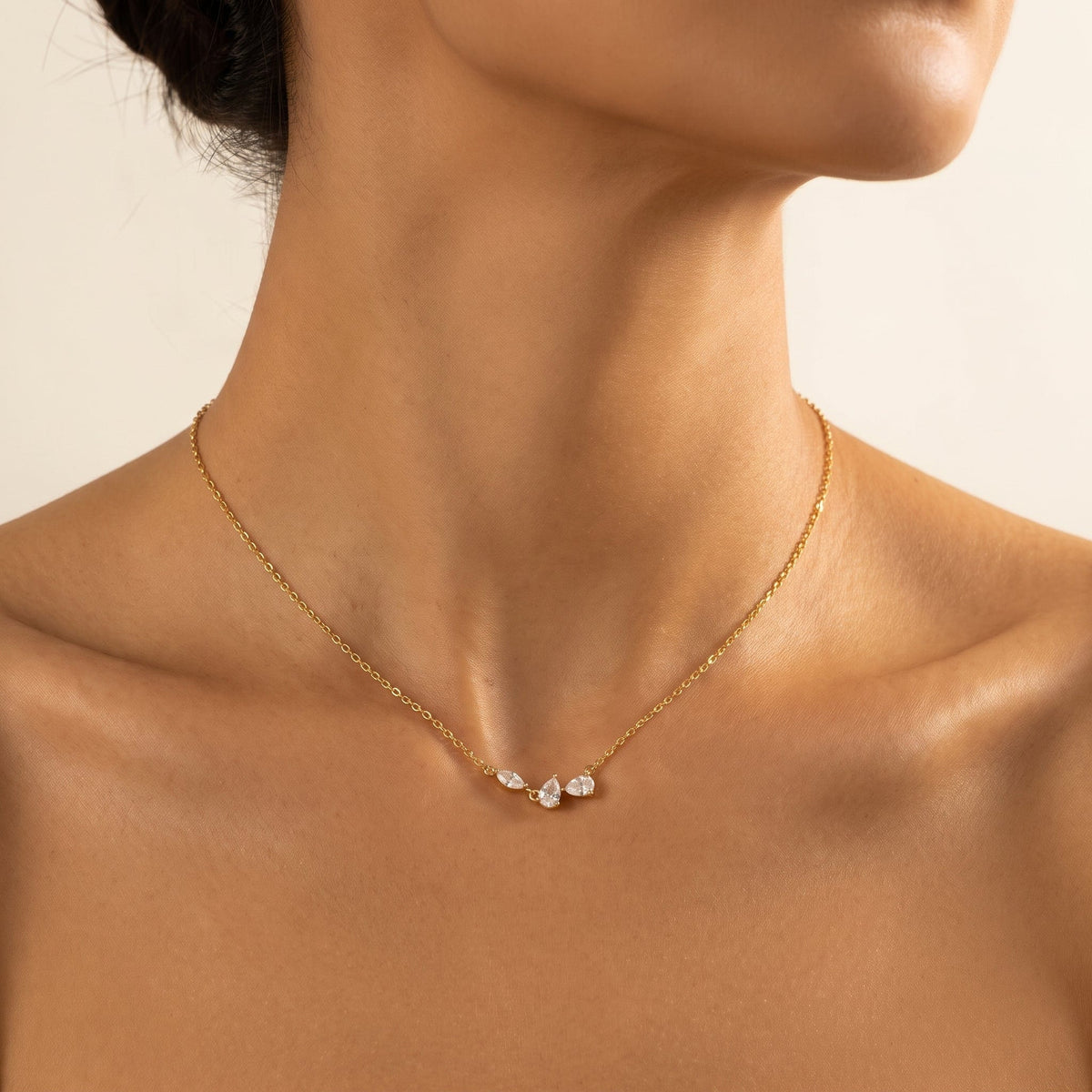 Wider view of a woman wearing the Rosalie pear cluster gold necklace at the collarbone