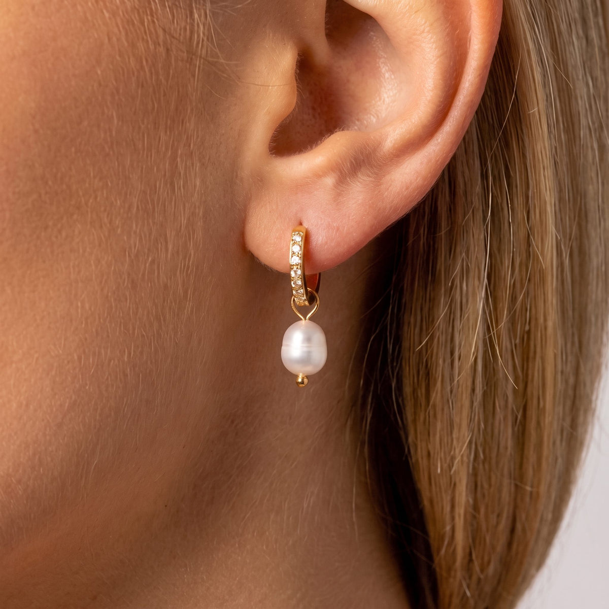 Woman wearing the Sara crystal-lined gold huggie with a hanging pearl drop