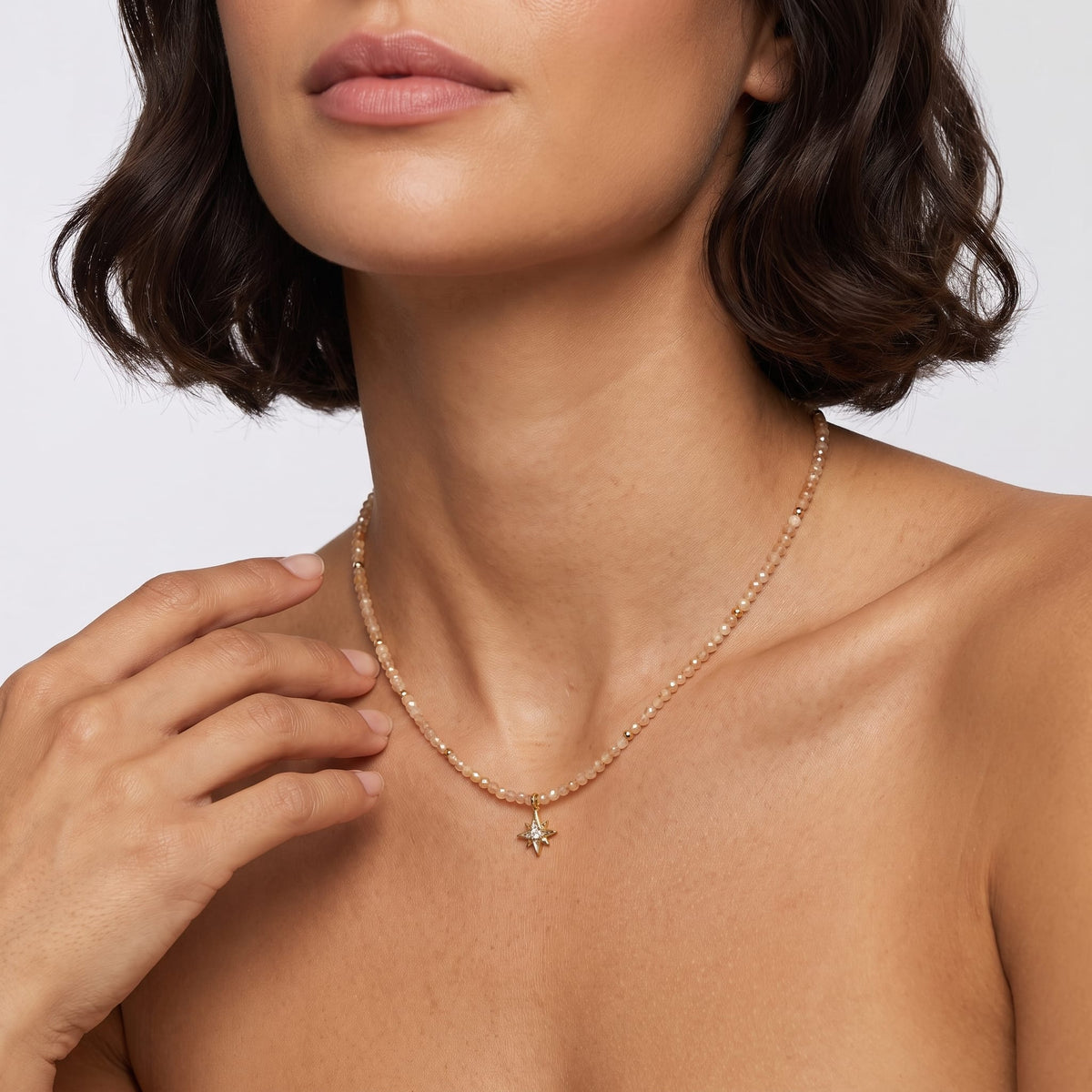Woman wearing the Selene star gemstone gold necklace at the collarbone while touching her neck against a white background