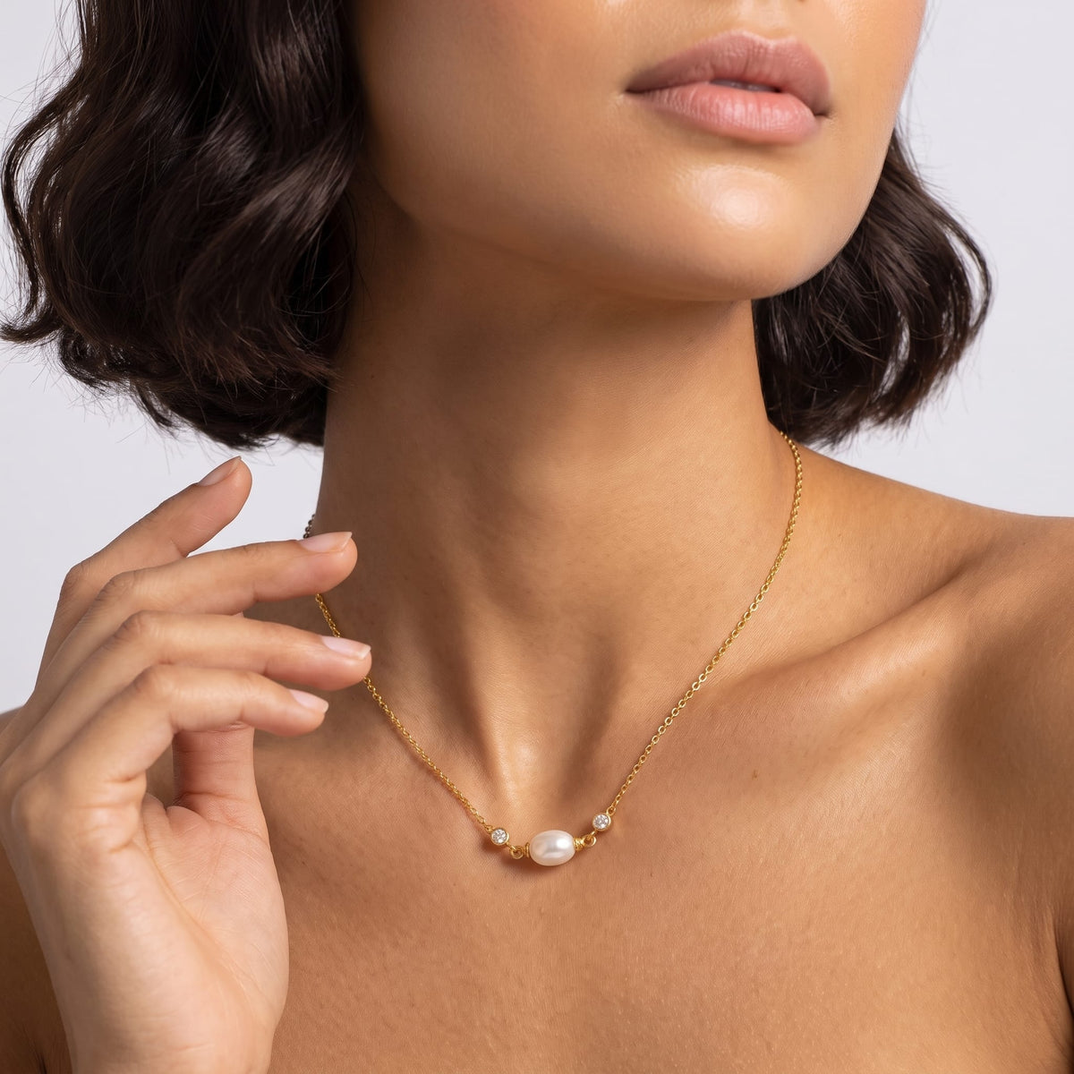Woman wearing the Serena single pearl gold necklace at the collarbone with short dark hair