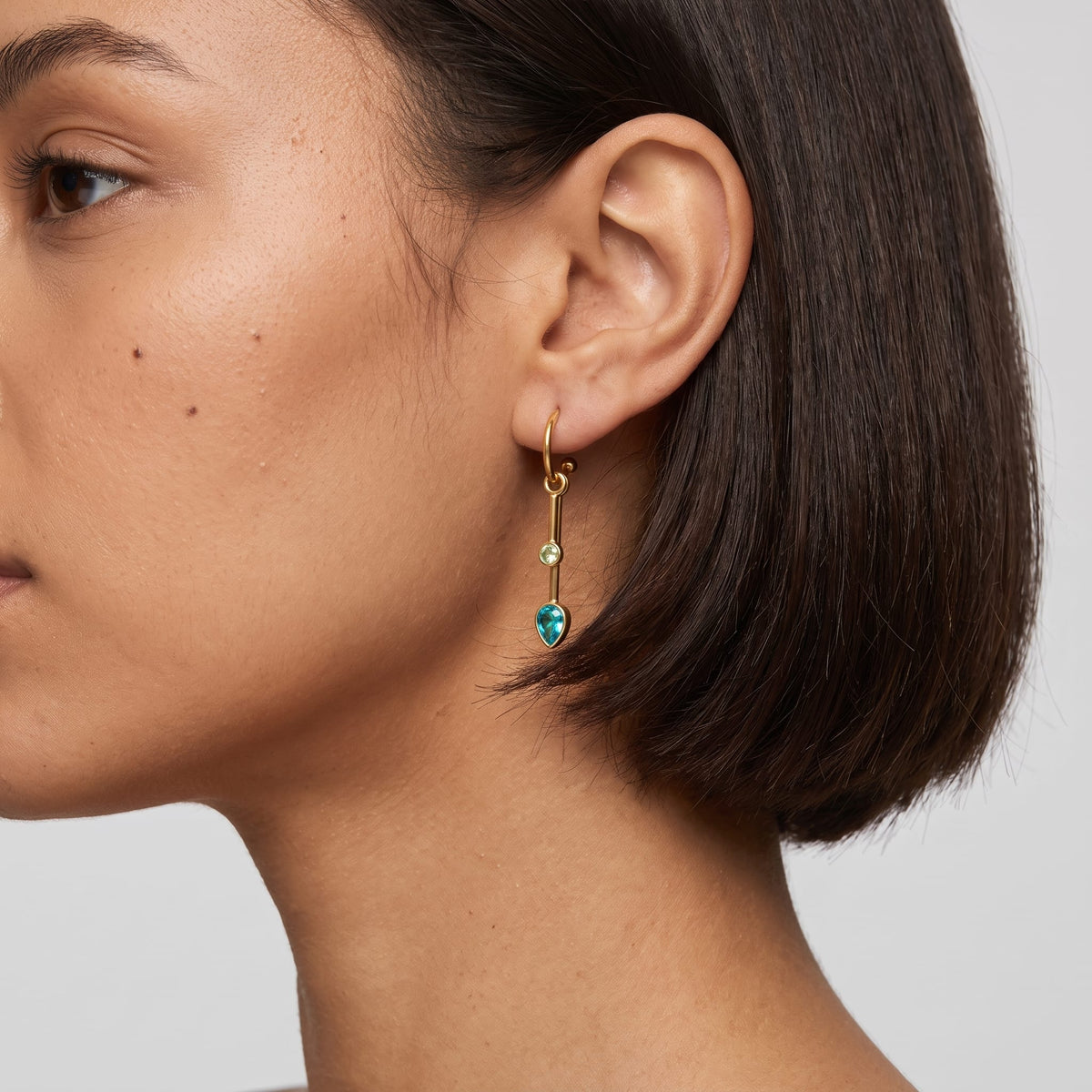 Woman wearing the Sixtine blue bar gold earrings on her ear, short dark haircut