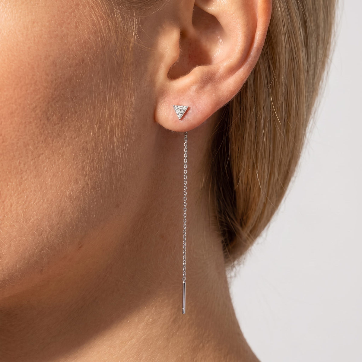 Woman wearing the Sofia Noir earring, a crystal triangle stud with a fine silver threader chain below the lobe
