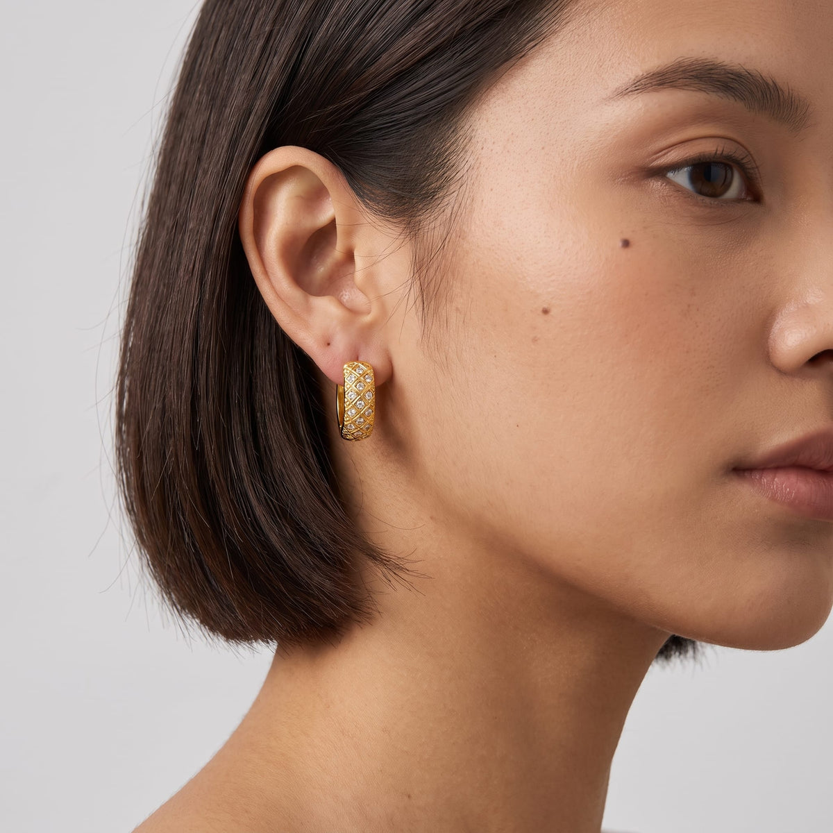 Woman wearing the Solène lattice hoop gold earrings on her ear showing her short dark hair