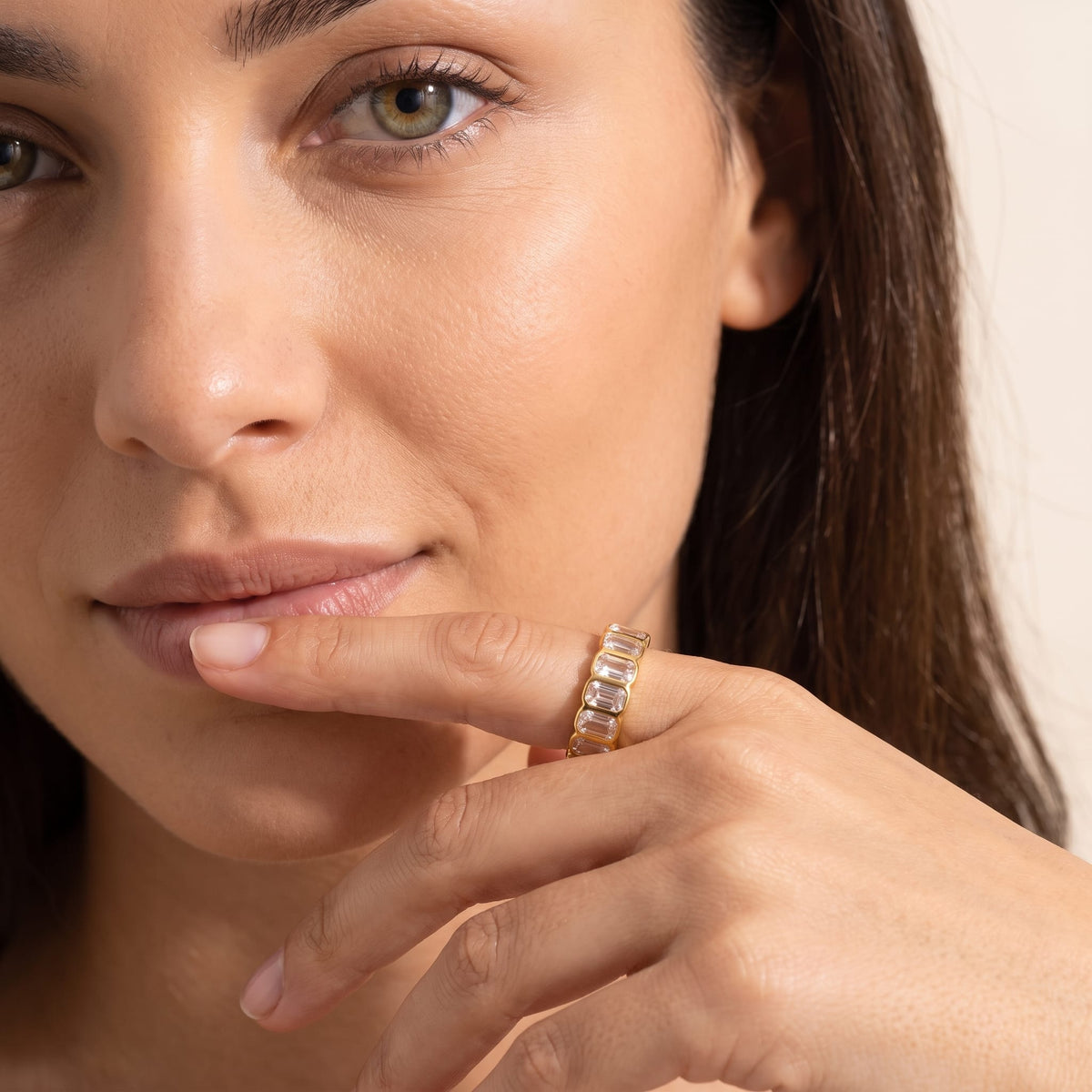 Woman wearing the Sophie baguette eternity gold ring on the hand touching her lower lip