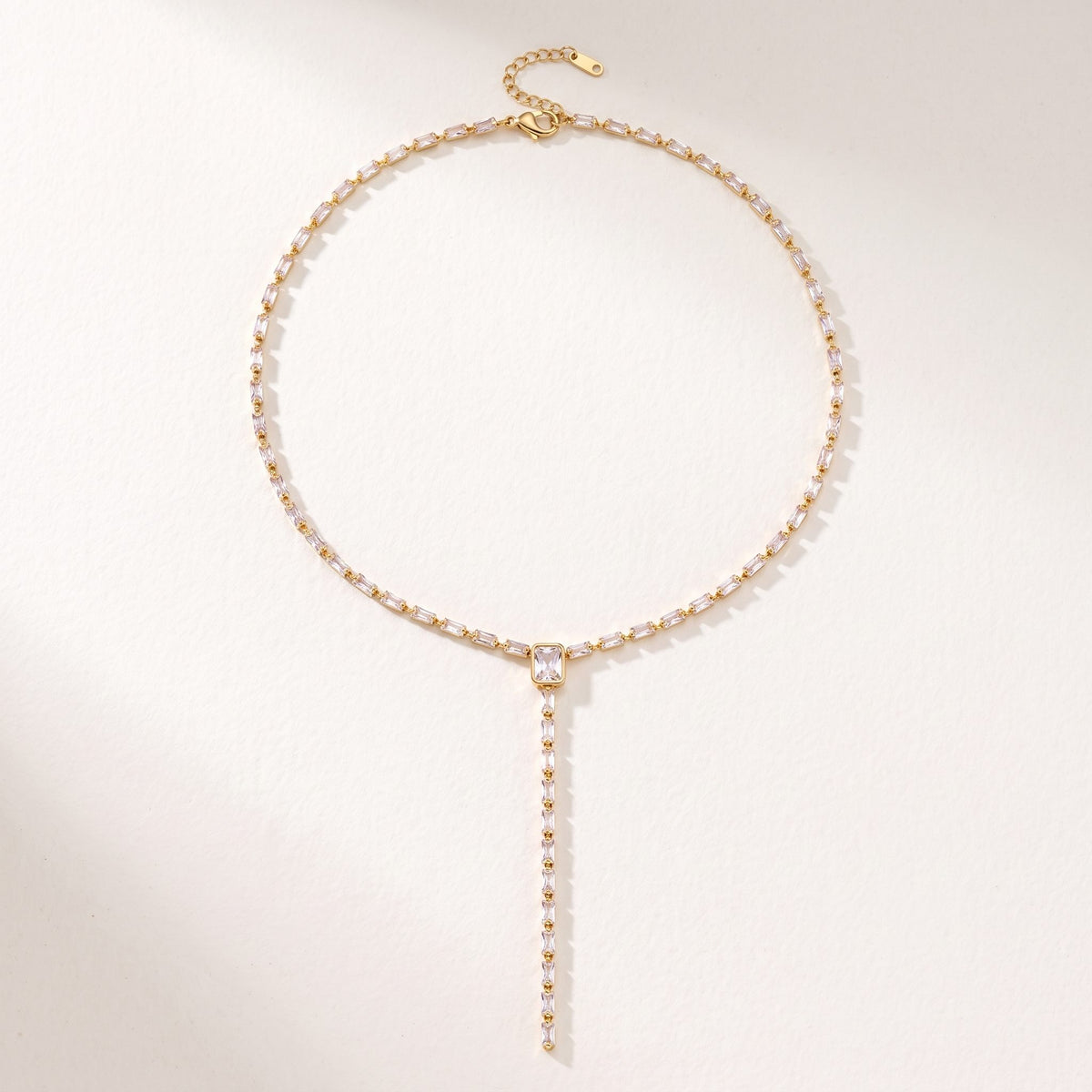 The Sophie baguette lariat gold necklace laid flat on an off-white surface