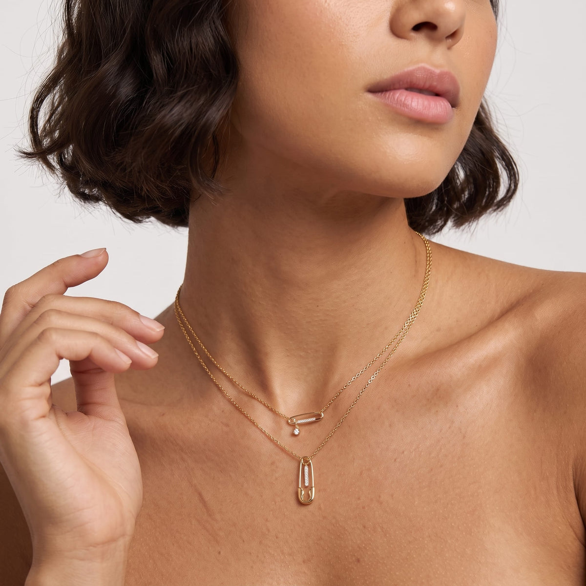 Woman wearing the Stella safety pin gold necklace at the collarbone with her hand raised