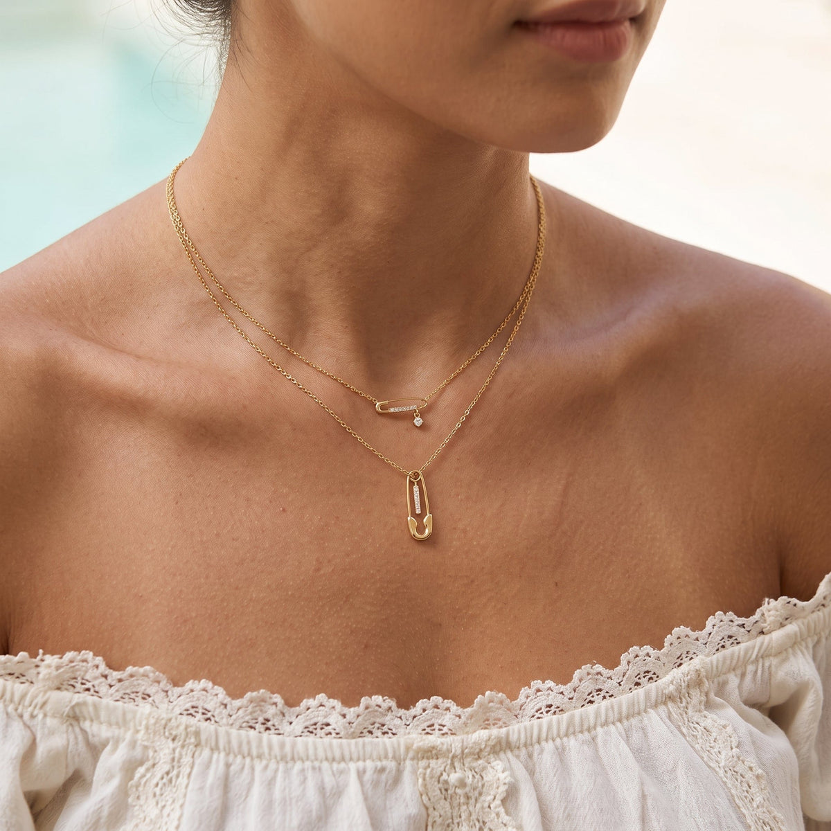 Wider view of a woman wearing the Stella safety pin gold necklace at the collarbone
