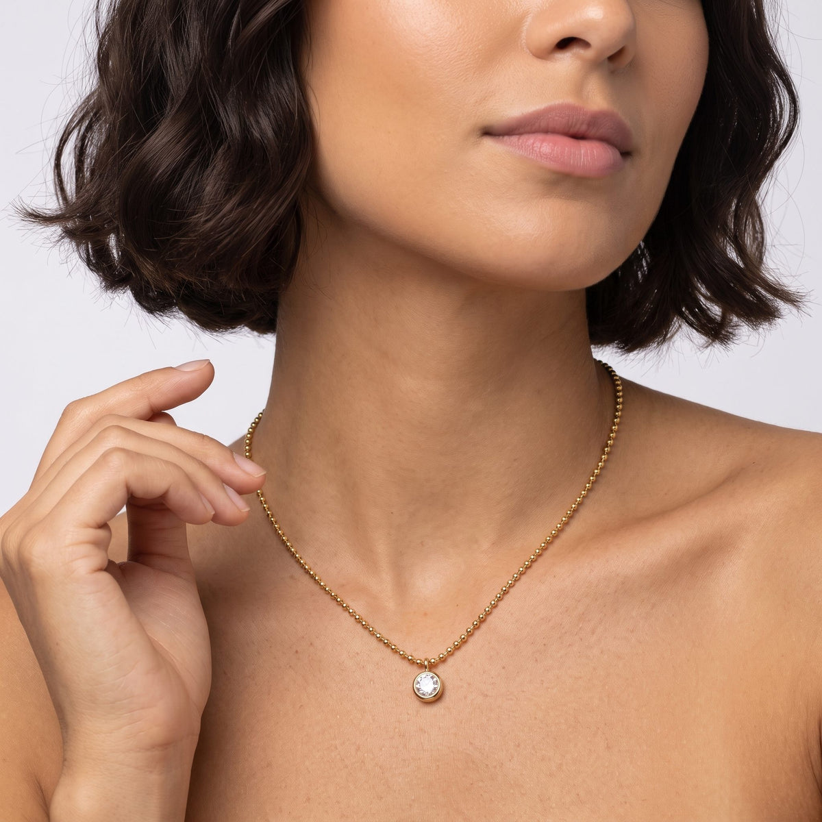 Woman with a dark bob wearing the Vida crystal bezel gold necklace, one hand raised near her neck