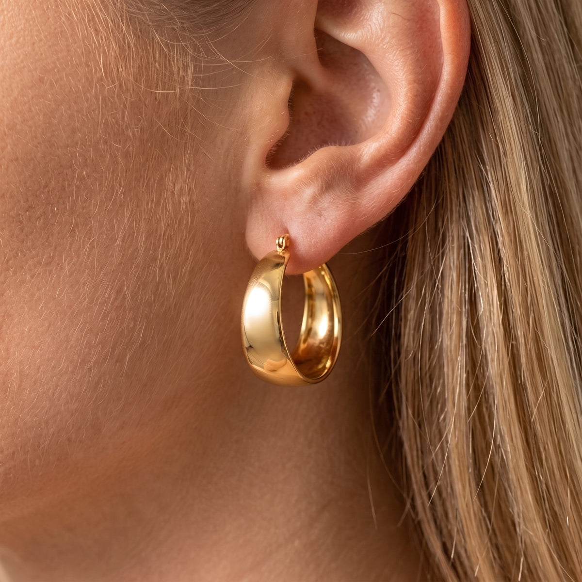 Woman wearing the Vivienne wide polished gold hoop that curves around the earlobe