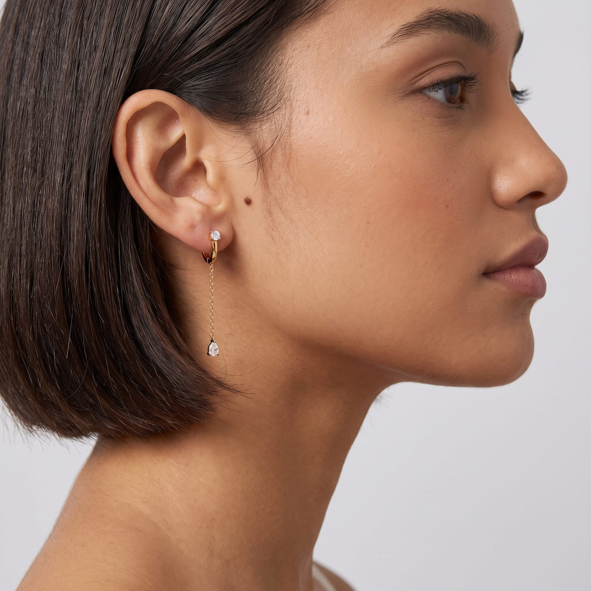 Woman wearing the Yvette chain drop gold earrings on the ear with short dark hair
