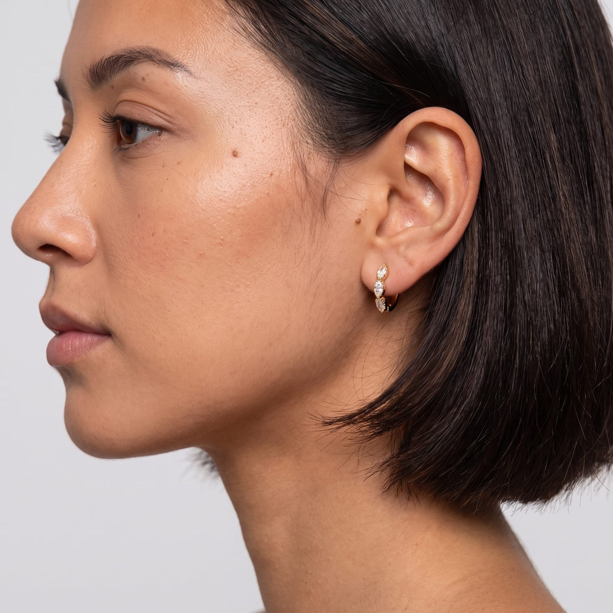 Woman wearing the Zoé marquise huggie gold earrings on the ear in profile with dark bob hair