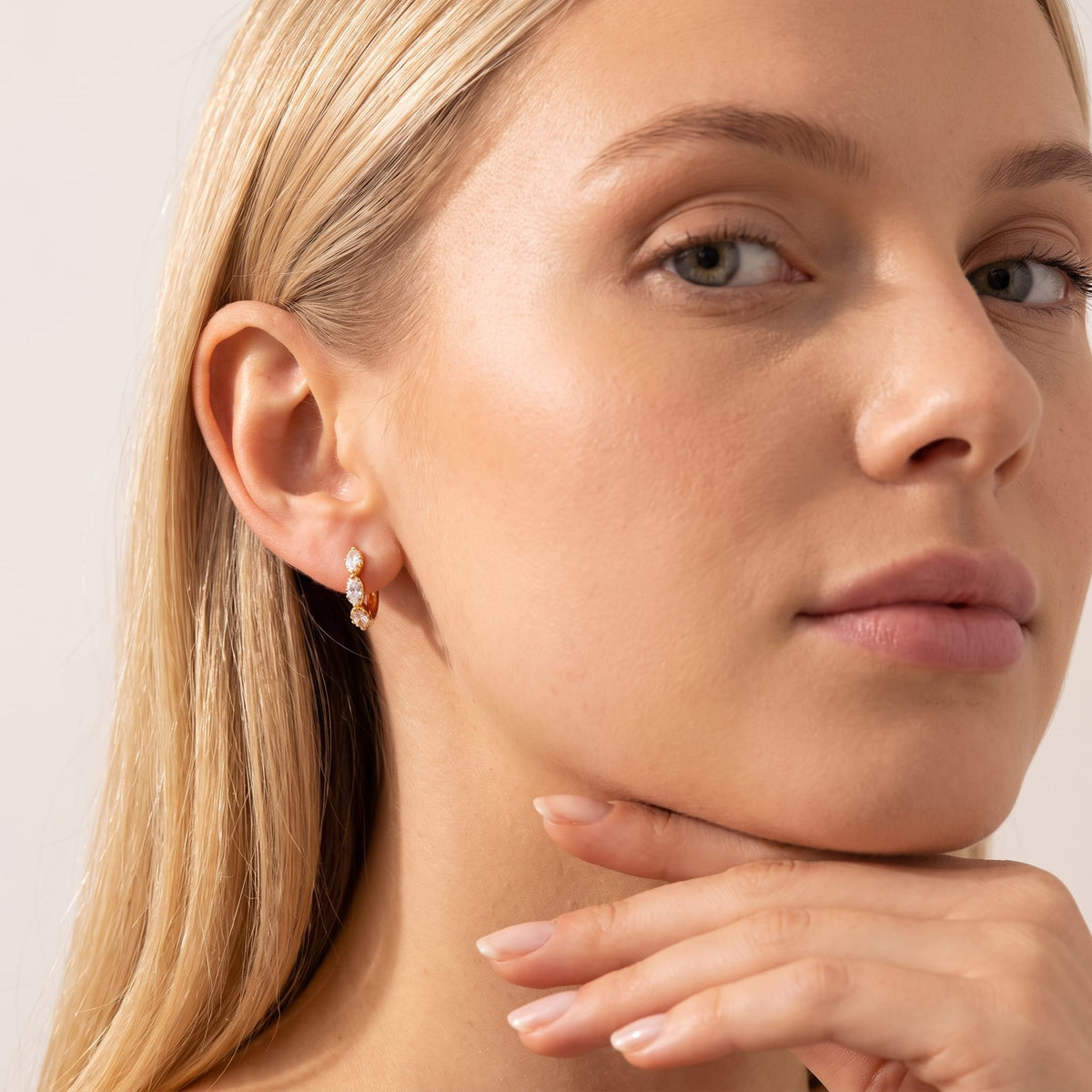 Woman wearing the Zoé marquise huggie gold earrings on the ear resting her chin on her hand